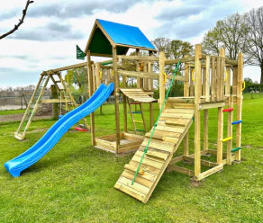 Großer hölzerner Spielturm mit Rutsche, Kletterwand und Wackelbrücke auf einer Rasenfläche